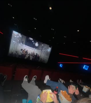 Mørk kinosal med en rad mennesker avbildet fra livet og ned med popcorn og baconsnacks